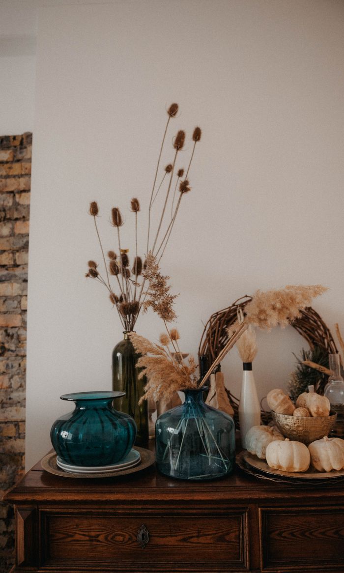 services-img Charming fall-themed arrangement with dried plants, glass vases, and pumpkins on a wooden table.