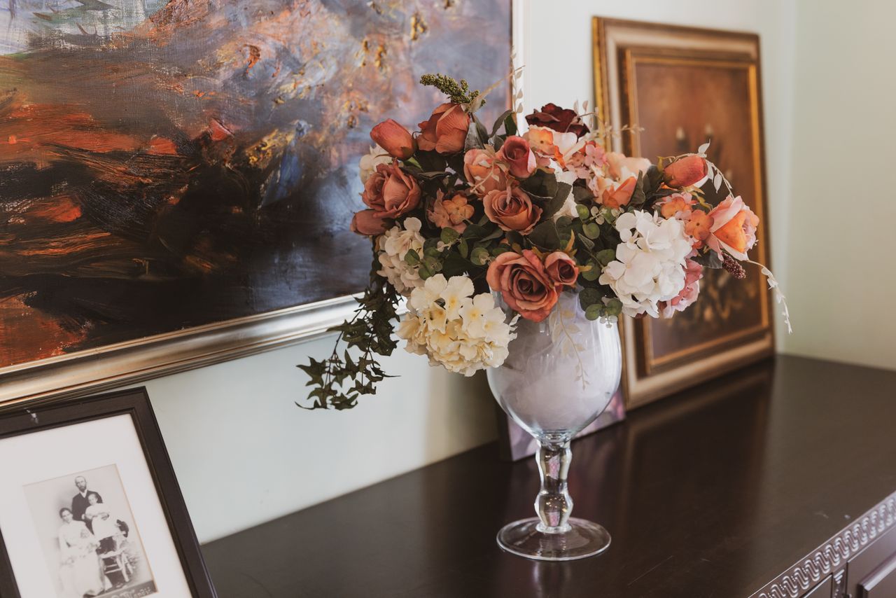 hero-img-01 Beautiful floral arrangement in a vase against a backdrop of artistic paintings, perfect for sophisticated decor.