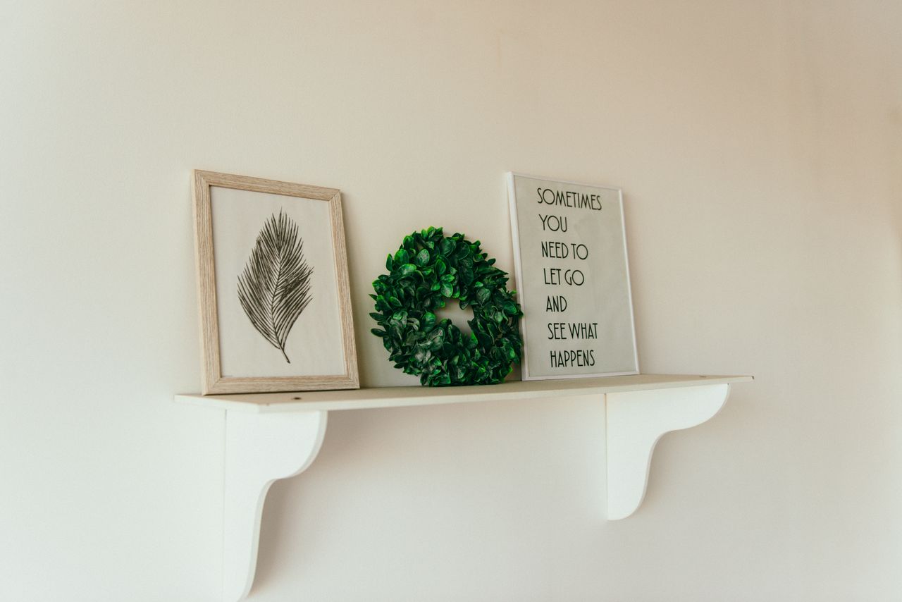 why-choose-us A minimalist shelf with framed art, a green wreath, and an inspirational quote.