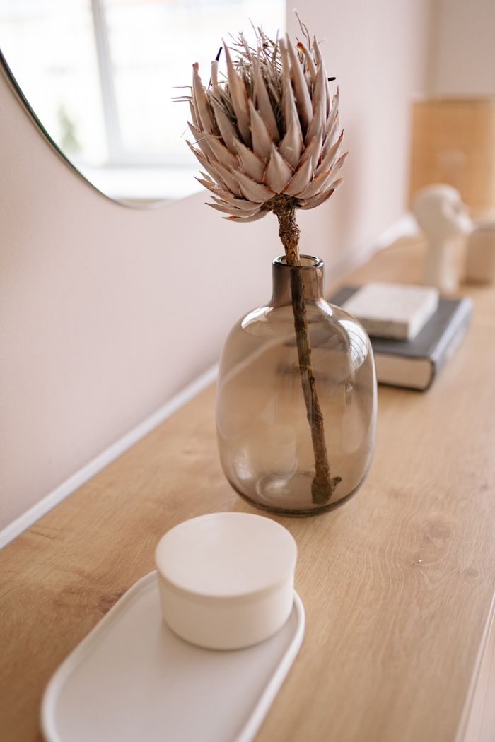 contact-img A close-up of a dried protea flower in a glass vase on a wooden table, capturing minimalist decor.