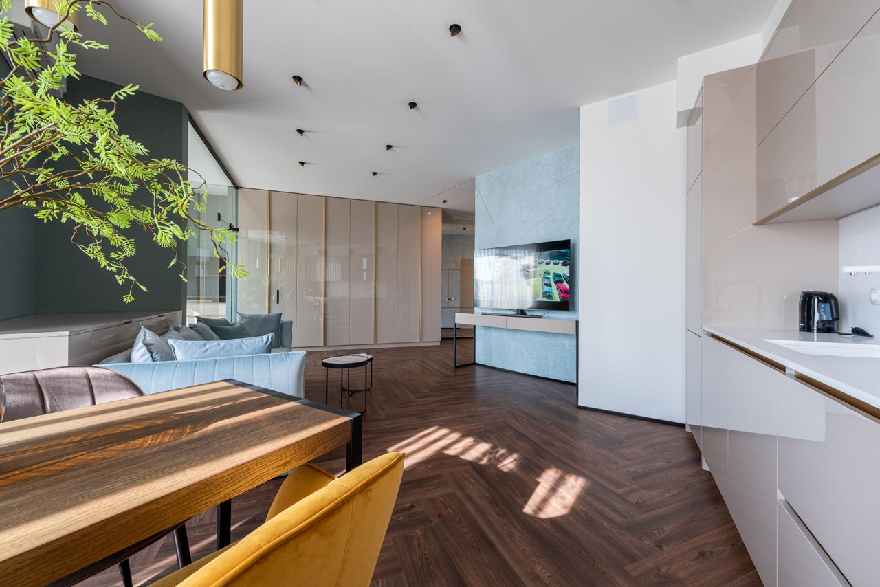 about-01 Kitchen interior with cabinets and wooden table placed near couch against wardrobe and TV set in modern apartment at home