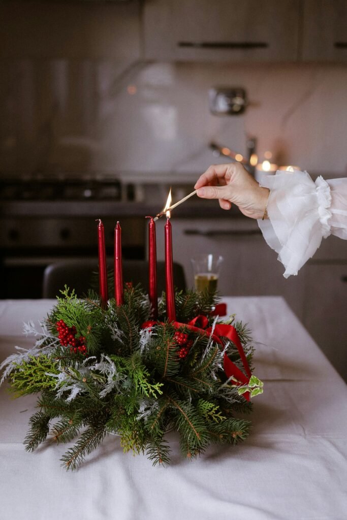 Christmas table centerpiece ideas, red taper candle cluster with greenery, berries, and ribbon being lit