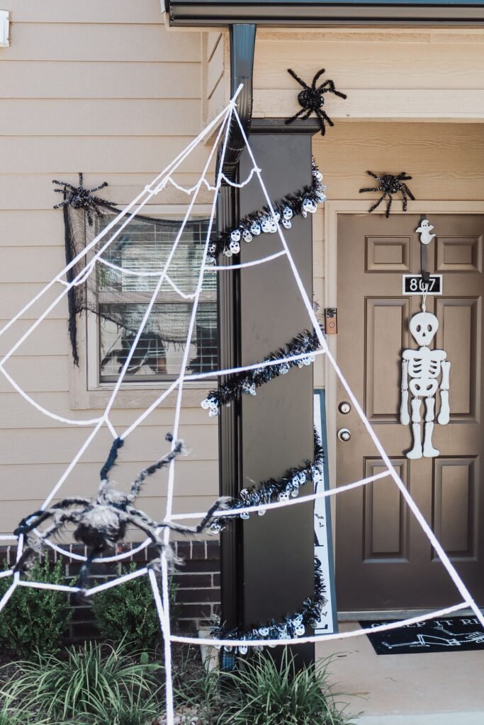 27 Stunning Halloween Door Decoration Ideas. Halloween front door decorated with giant spider web, black spiders, and skeleton garland